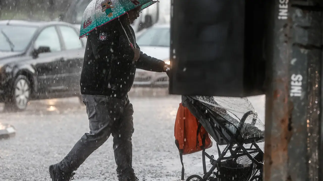 Un hombre lleva un carrito de beb&eacute; mientras se protege de la lluvia con un paraguas | Rober Solsona / Europa Press